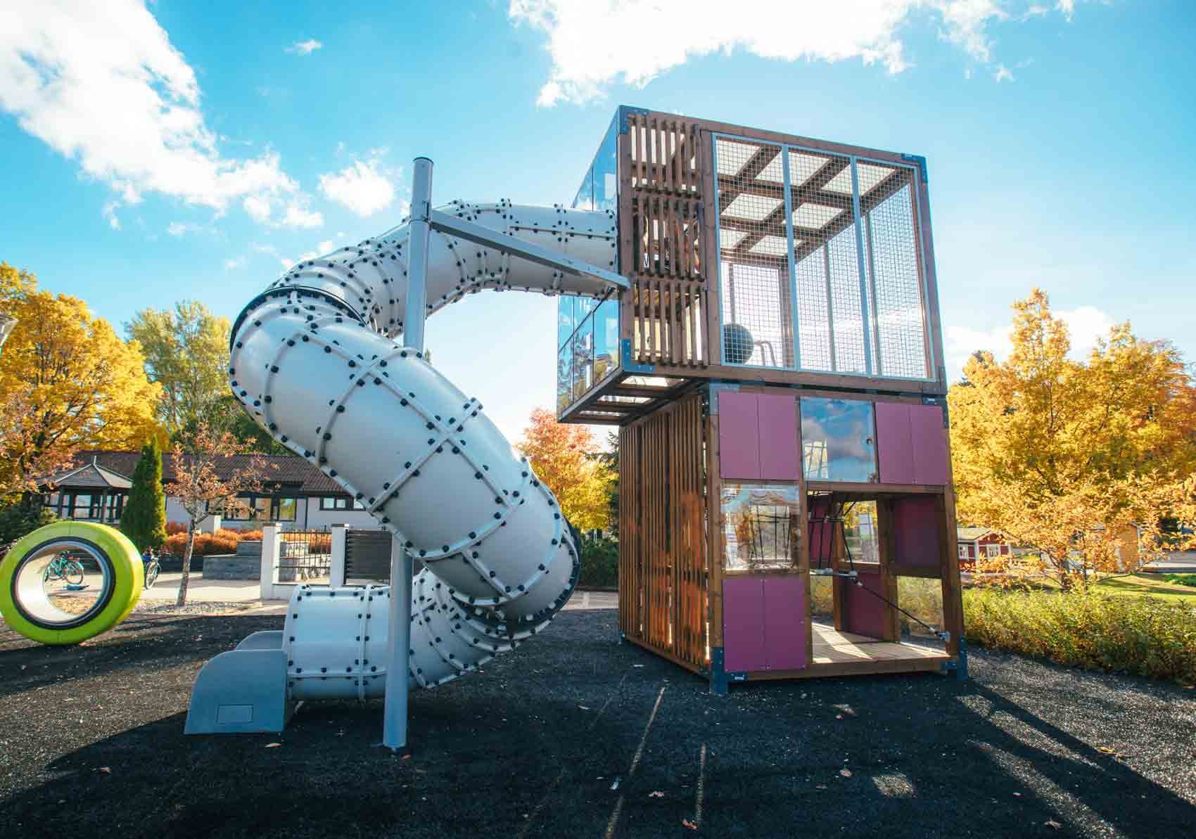 Modern play tower made of Nordic wood with tube slide and colorful panels