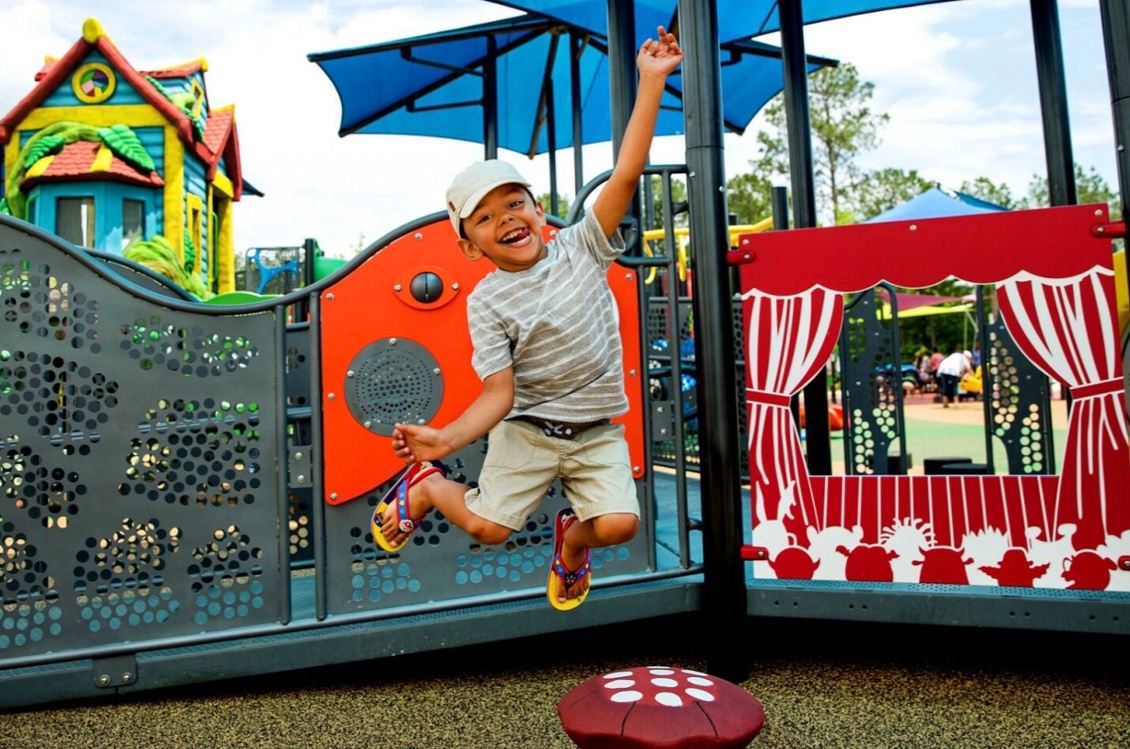 Excited boy jumping in front of commercial playground equipment