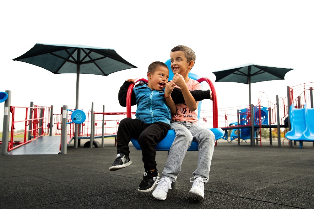 Kids playing on sensory spinning seat in front of commercial playground equipment