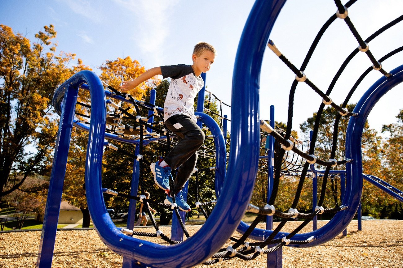 Boy running across rope race net commercial playground structure